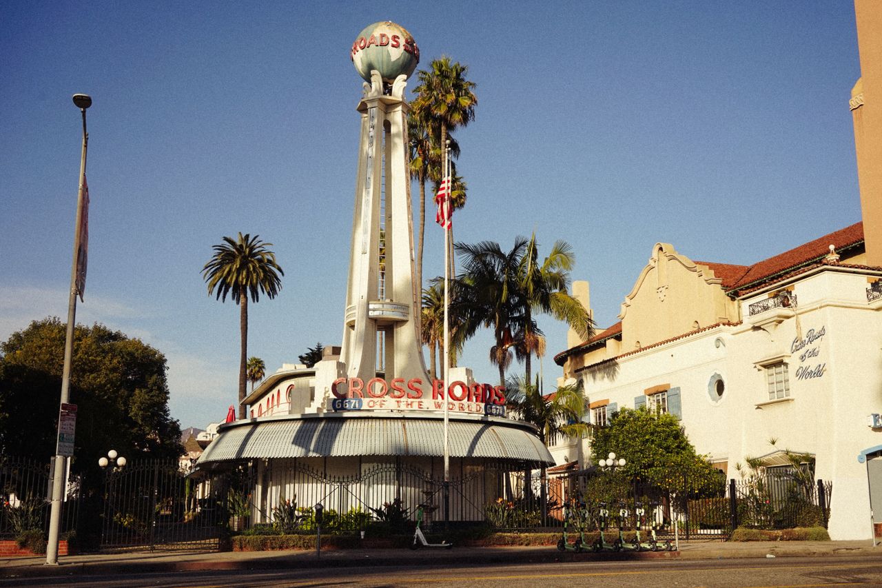 Home Vintage view of the iconic Crossroads of the World landmark in Los Angeles, featuring palm trees under a clear sky.