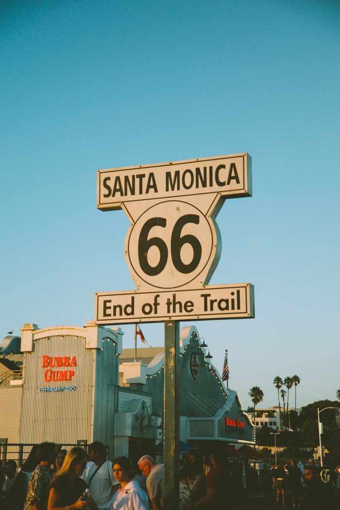 Iconic Route 66 end sign in Santa Monica at sunset with Bubba Gump in the background.